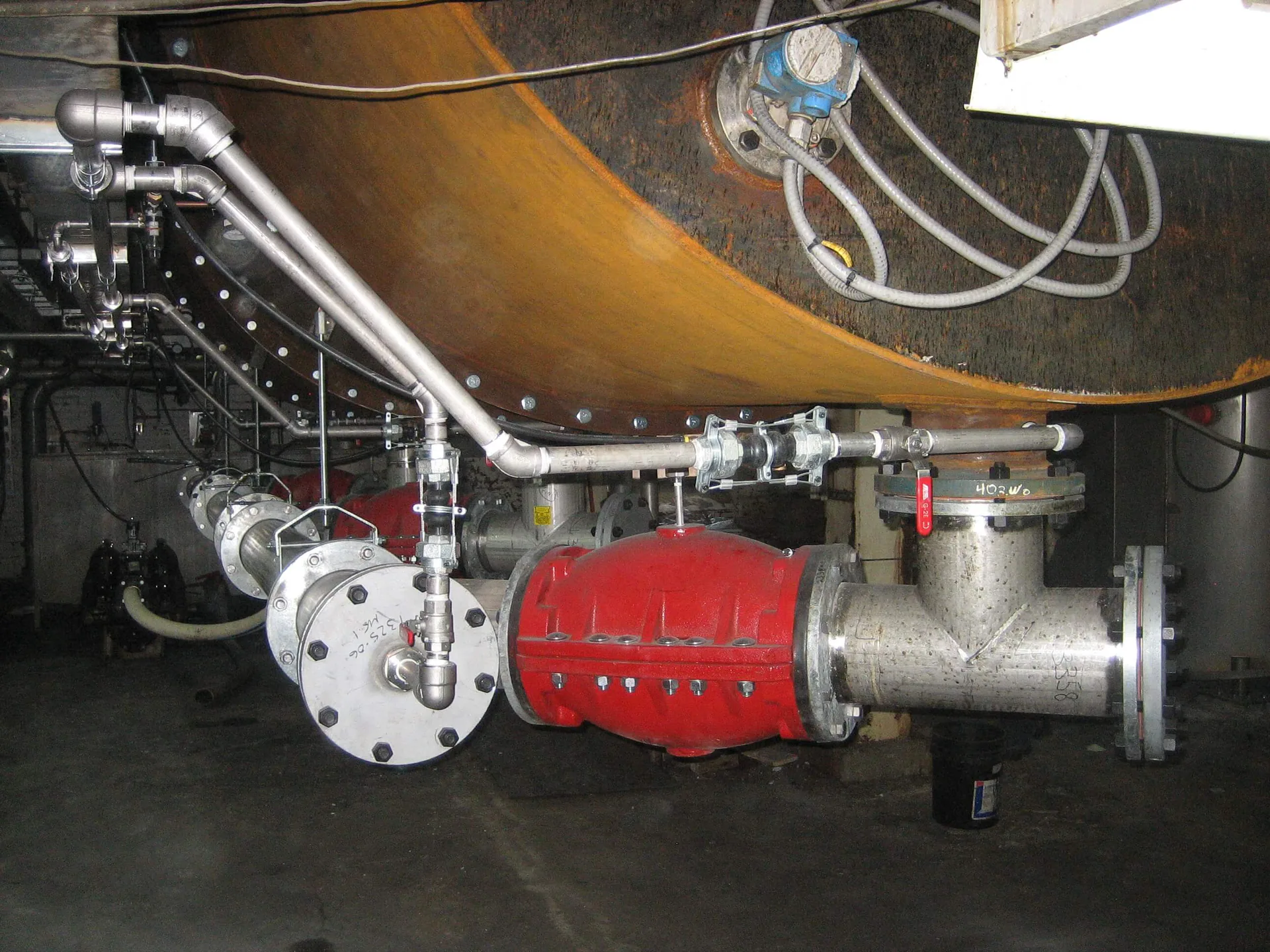 Collecteur de tuyauterie industrielle en acier inoxydable avec vannes et grande connexion à bride sous une surface cylindrique.