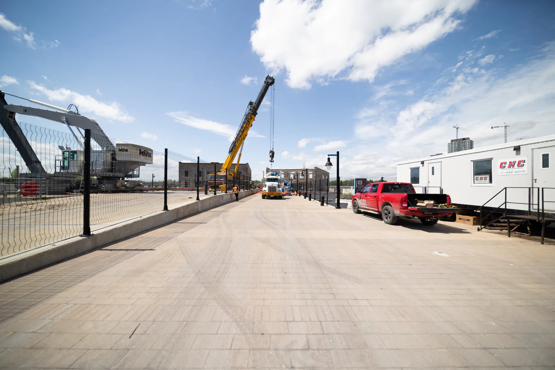 Vue large d’un chantier marqué CNC avec remorque, camionnette, grue mobile et équipement de transport lourd.