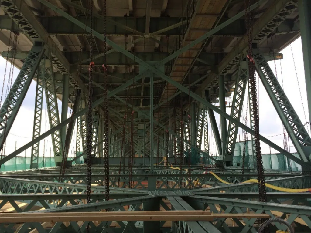 Dessous de la charpente d’acier d’un pont avec palans à chaîne et filets de protection.
