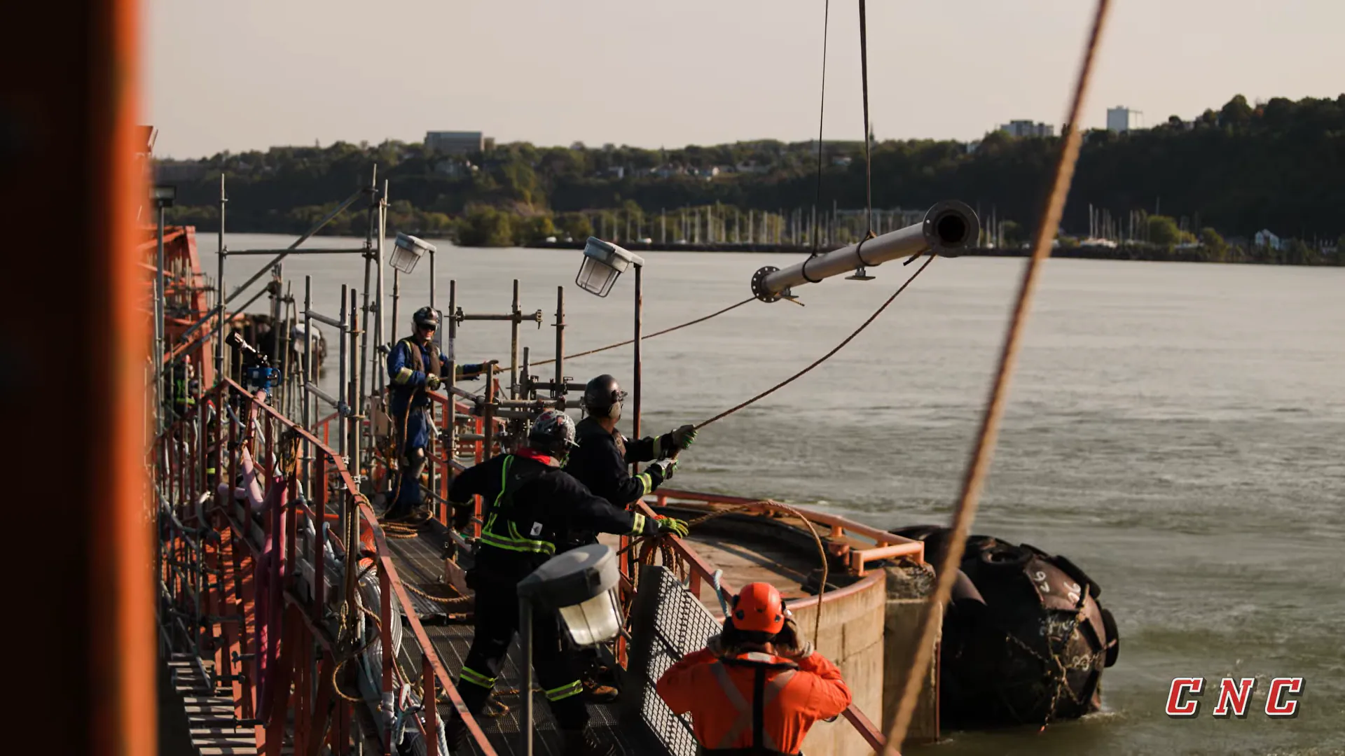 Travailleurs guidant une section de tuyauterie suspendue au-dessus du quai de Valero, à Lévis.