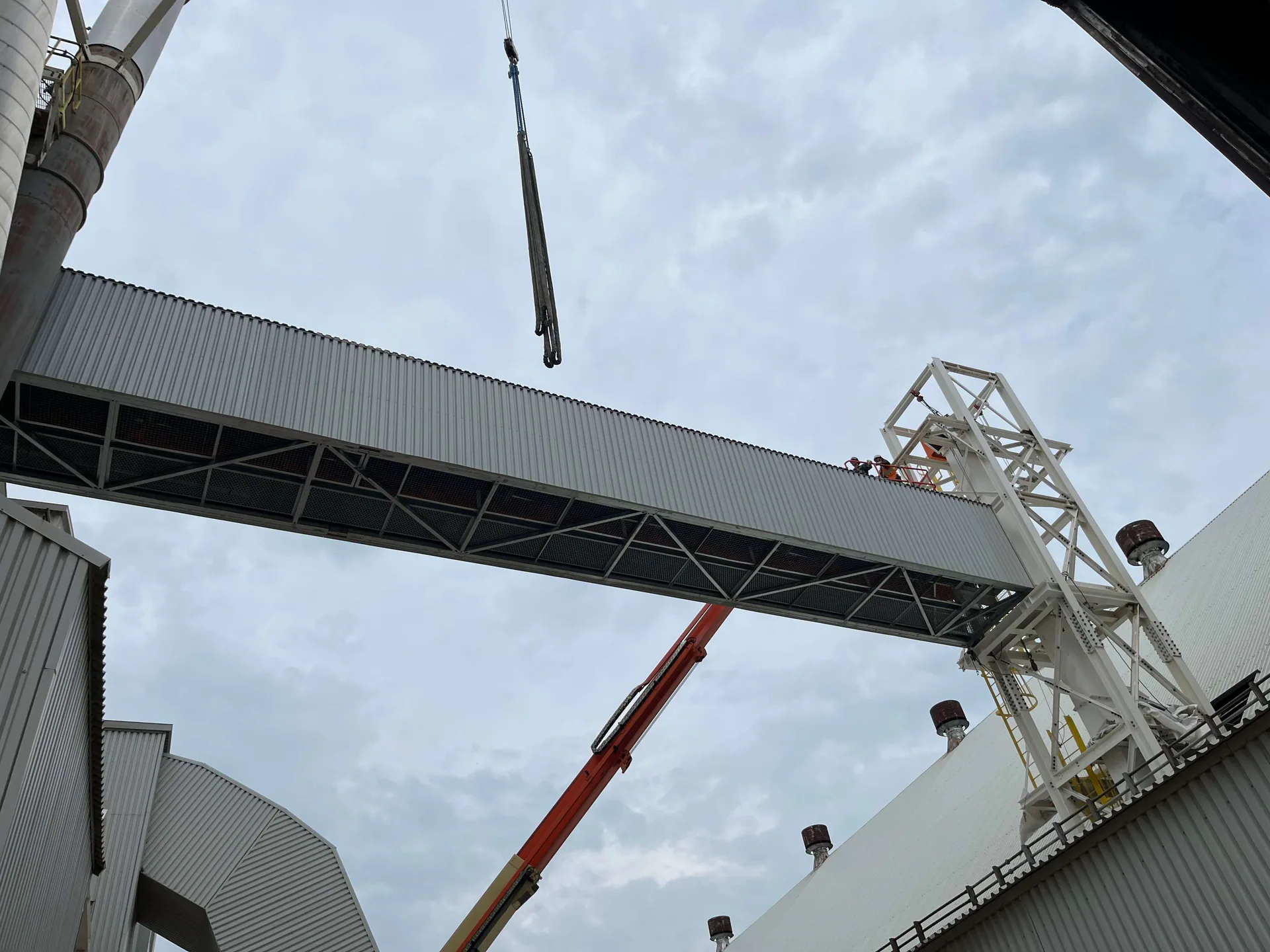 Galerie d’acier fermée installée entre deux bâtiments industriels, avec une grue et deux travailleurs sur le dessus.