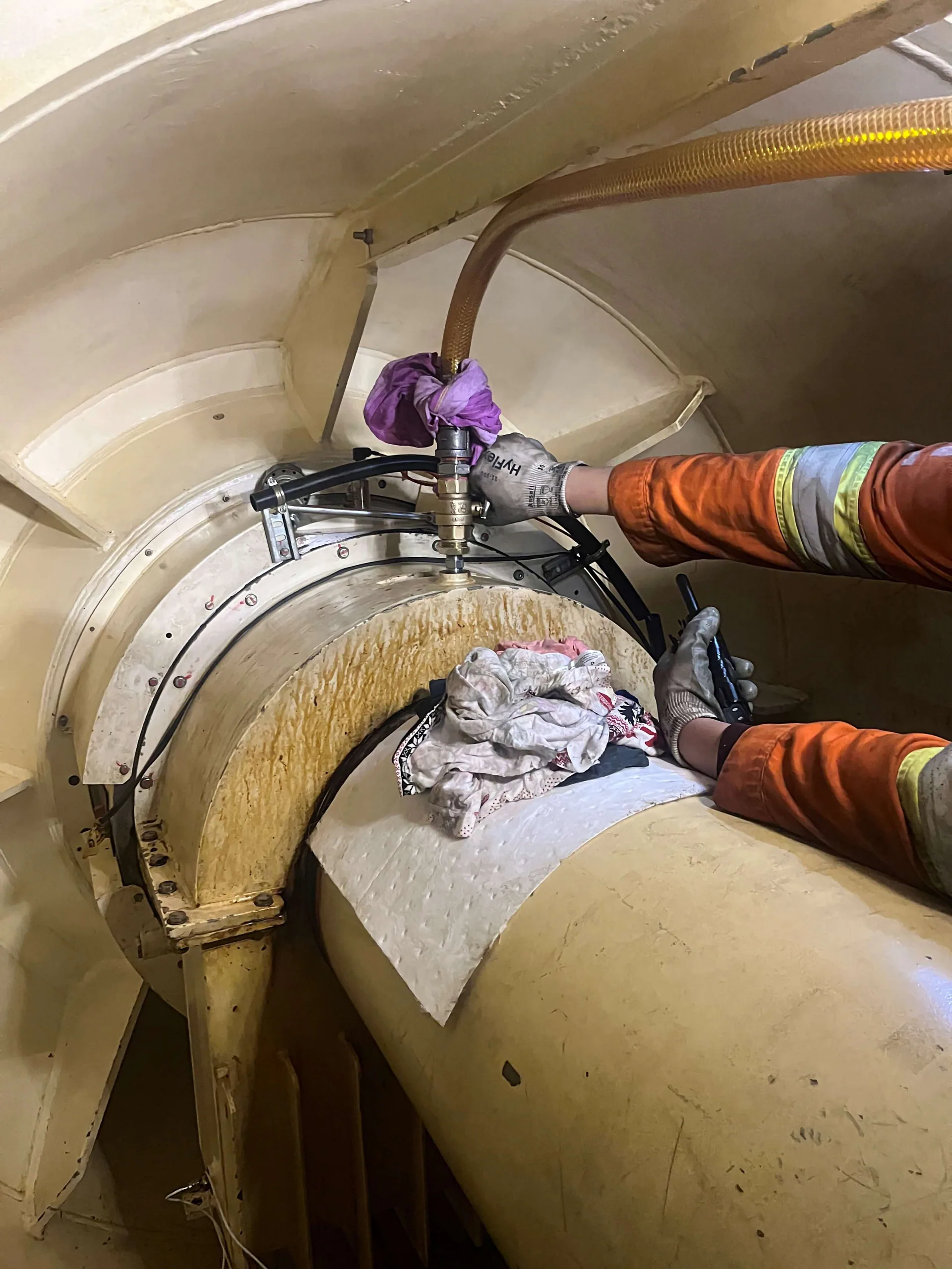 Vue rapprochée de mains gantées actionnant un outil hydraulique et des flexibles sur un assemblage circulaire de machine industrielle.