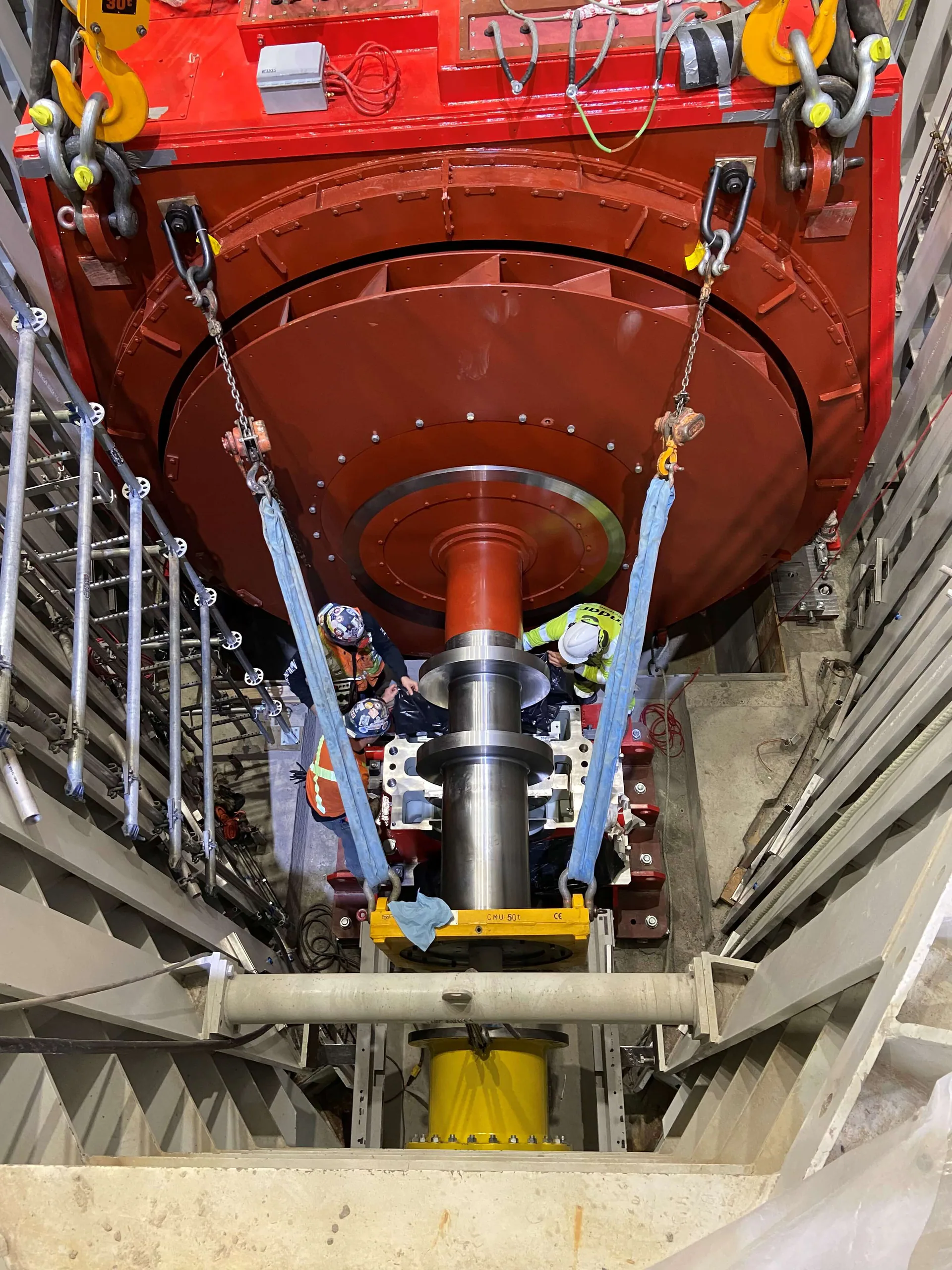 Vue plongeante de travailleurs près d’un imposant rotor rouge ou assemblage de génératrice et d’un arbre poli dans une centrale.