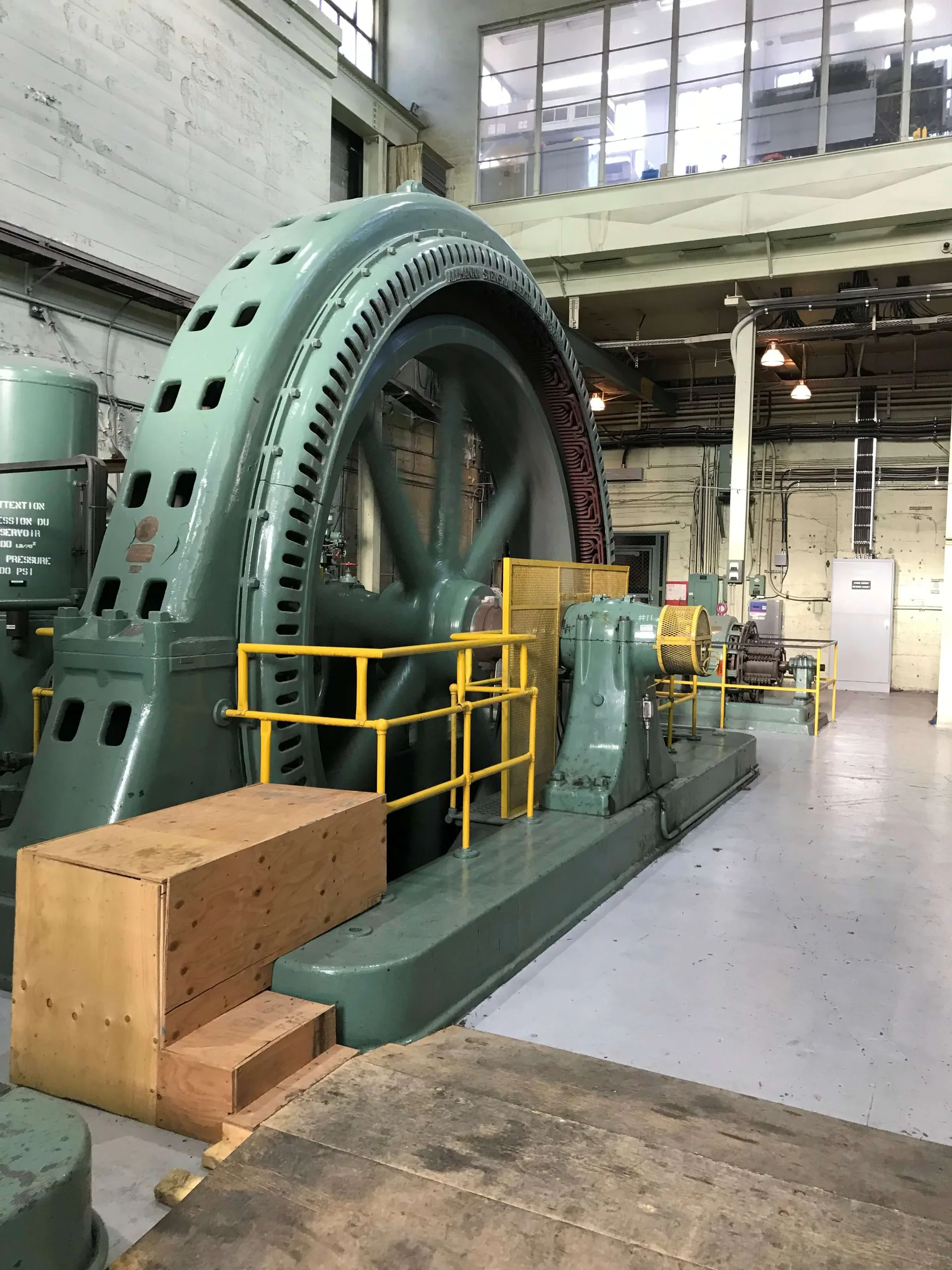 Grande génératrice historique verte ou machine rotative exposée dans une centrale avec garde-corps jaunes.