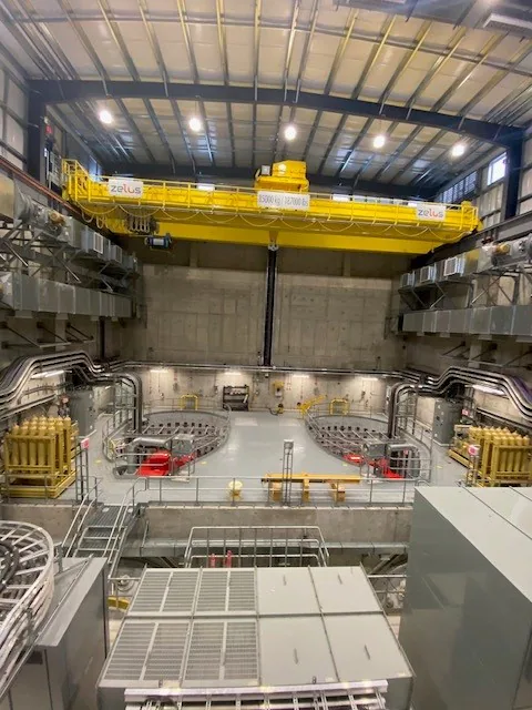 Vue large de l’intérieur d’une grande salle de type centrale avec deux ponts roulants jaunes et des baies de machinerie.