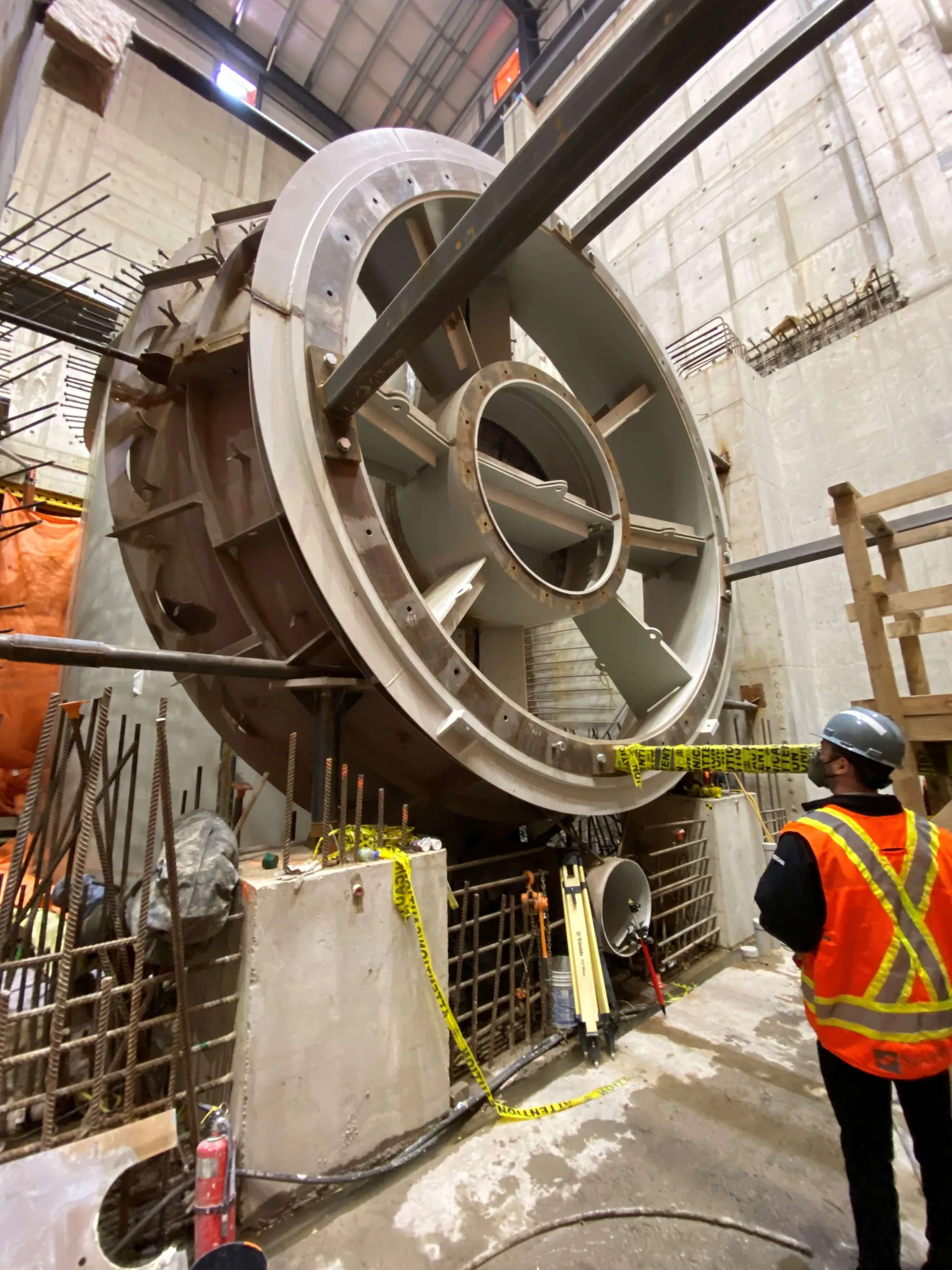 Grand carter circulaire de machine en acier positionné dans une centrale en béton pendant qu’un travailleur observe.