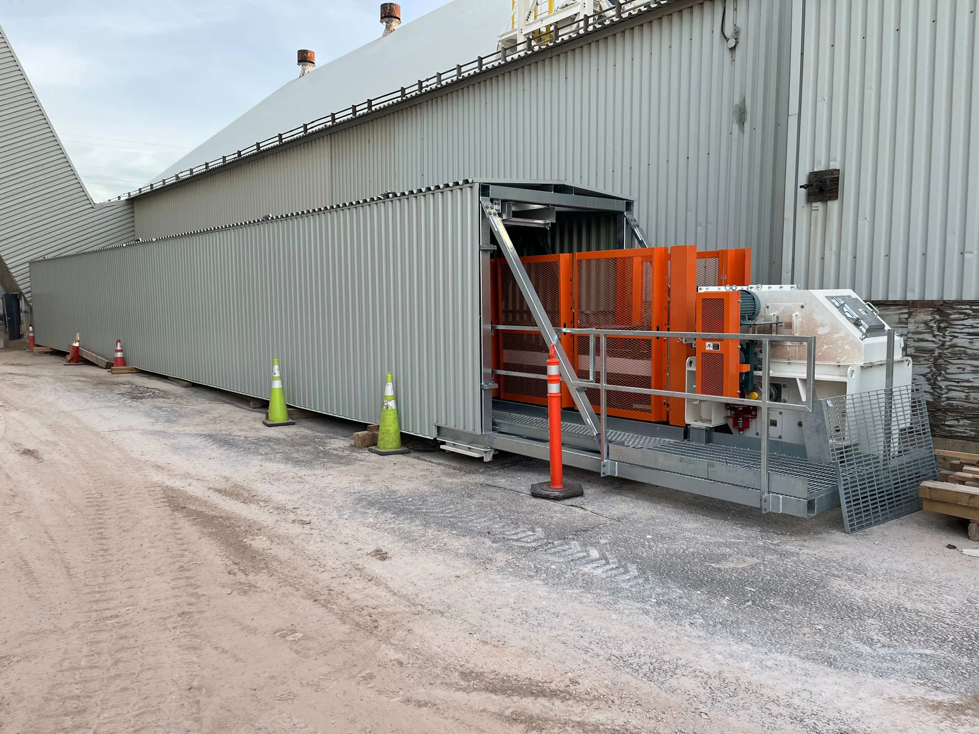 Galerie d’acier fermée terminée au sol près d’une usine, avec un entraînement orange protégé ou un équipement mécanique à une extrémité.