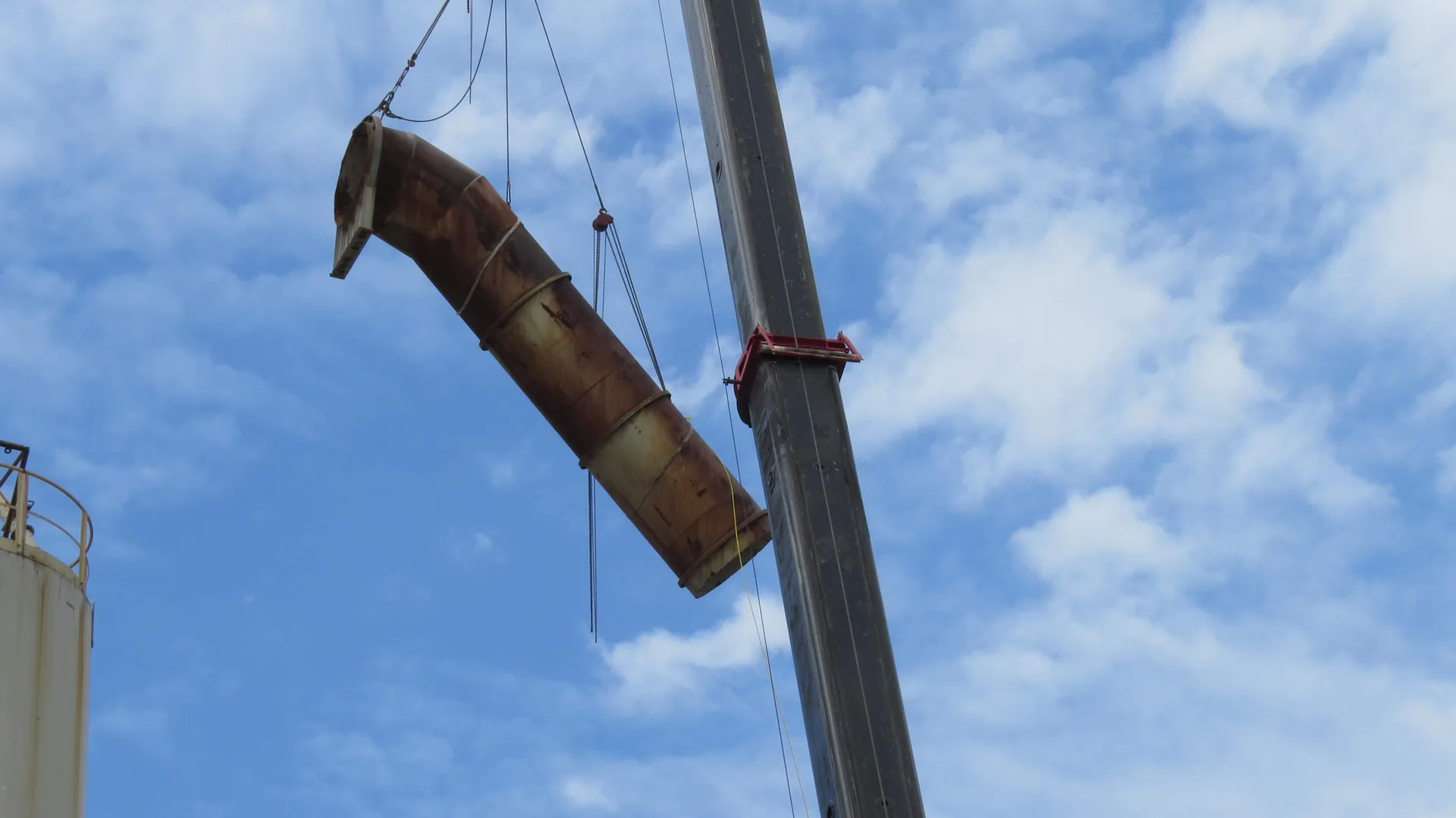 Grande section courbée et patinée de conduit ou d’enveloppe industrielle suspendue à une grue devant le ciel.