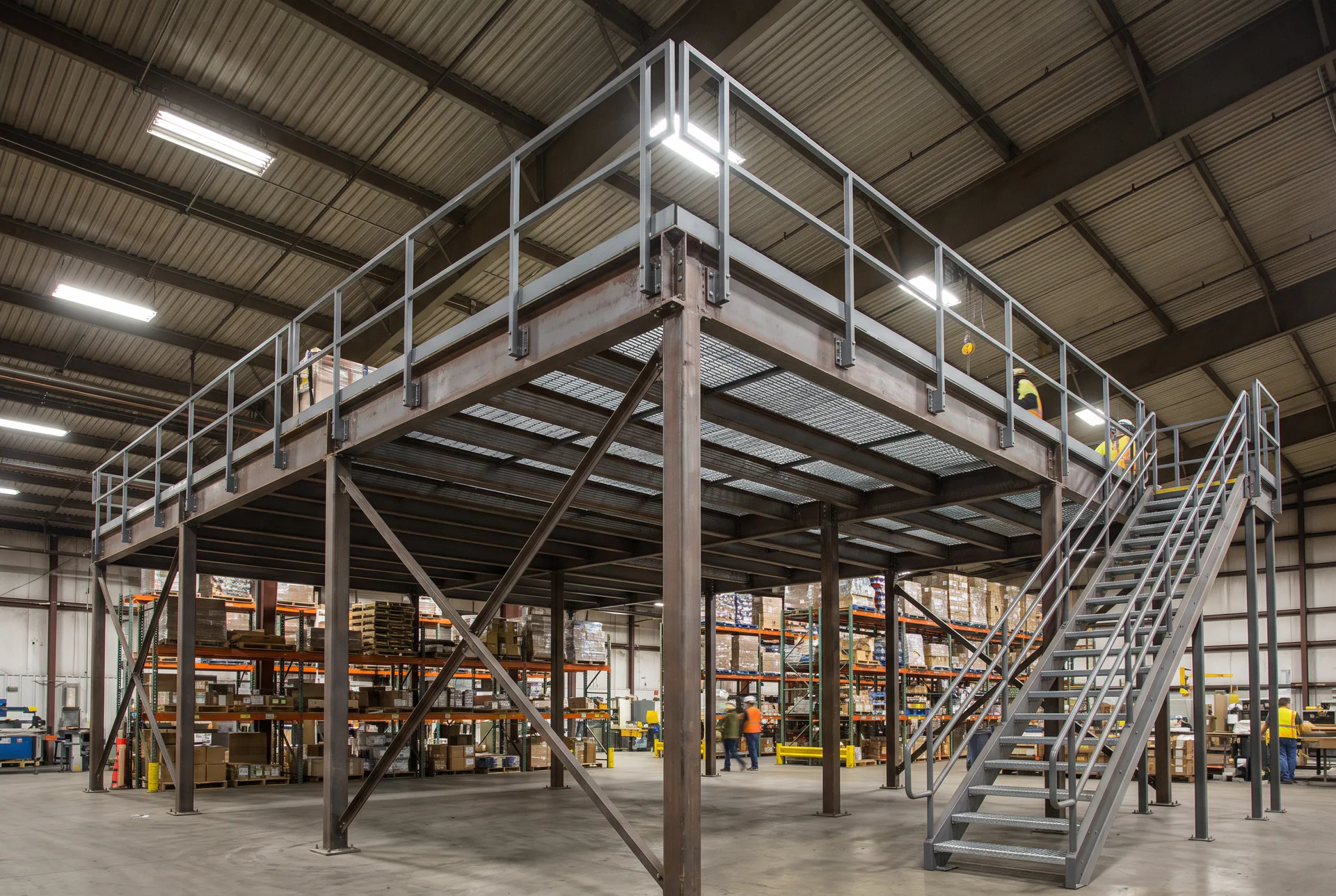 Mezzanine industrielle générique en structure d’acier boulonnée : plateforme sur colonnes, garde-corps et escalier d’accès, sans client ni installation identifiable.